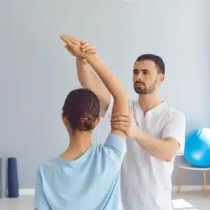 A physical therapist gently guides a female patient's raised arm through an assisted shoulder mobility exercise as part of her rotator cuff surgery recovery timeline
