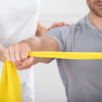 Patient pulls resistance band during therapy while orthopedic urgent care guides shoulder strengthening exercises safely