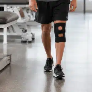 A close-up shows a person walking indoors with a supportive knee brace, illustrating can you walk with a torn ACL during everyday movement