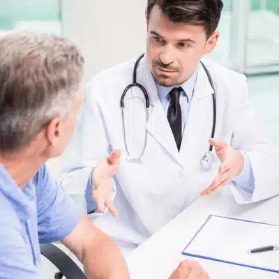 Doctor explains benefits of patient education to older man during clinic consultation, using notes today