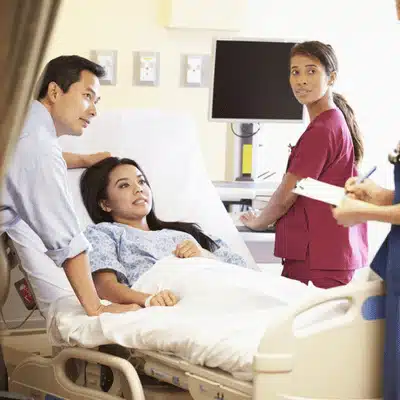 Patient rests in hospital bed while family and nurses discuss care plan during rounds today