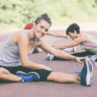 Smiling athlete stretches hamstring during group warmup, practicing sports injury prevention with consistent flexibility exercises