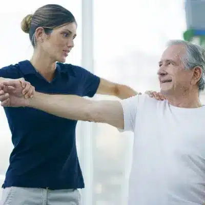Physiotherapist guides senior through shoulder exercises as part of bursal surface tear treatment program rehabilitation
