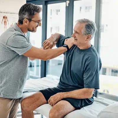 therapist guiding an older patient through gentle shoulder movement after evaluation by an orthopedic shoulder surgeon.