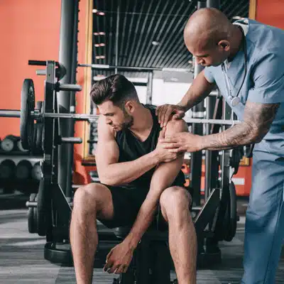 Physiotherapist examines athlete's shoulder at gym bench, assessing rotator cuff strain and treatment plan today