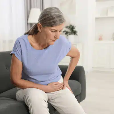 Senior woman sitting on couch holding hip in pain considering outpatient hip replacement