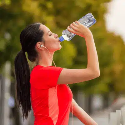 Female runner drinks water from bottle during workout rest break, maintaining hydration and endurance outdoors