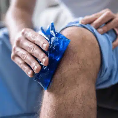 A person holds an ice pack against a sore knee after a knee examination to reduce swelling