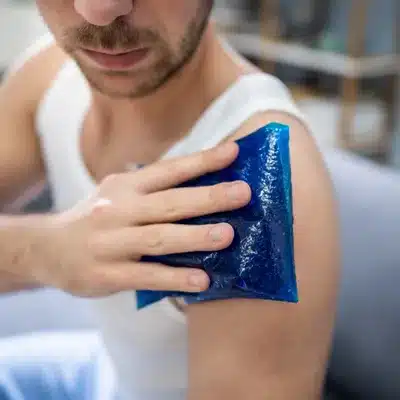 Patient applies ice pack on injured shoulder during initial bursal surface tear treatment at home