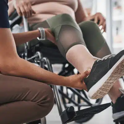 Physical therapist assists patient in wheelchair after total joint replacement to check joint movement