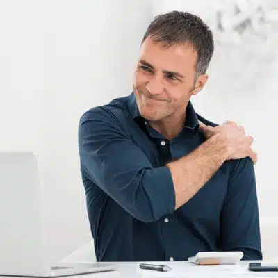 Man rubs shoulder at desk showing discomfort before visiting orthopedic urgent care for assessment