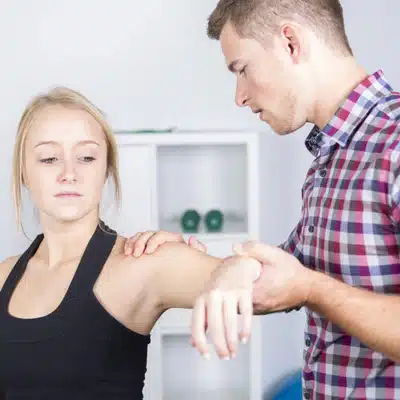 Physical therapist evaluates patient’s shoulder mobility, guiding arm movement during rehabilitation session in clinic today.