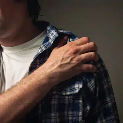 Man in plaid shirt clutches aching shoulder, considering bursal surface tear treatment with specialist consultation