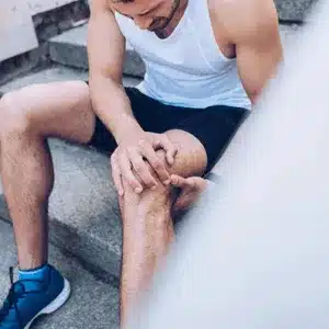 Man sits on stairs with visible knee pain after an intense workout session