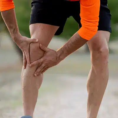 Athlete in bright sportswear grabs painful knee outdoors mid-run, indicating sudden strain or overuse injury