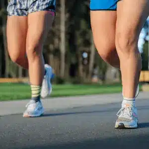 Two women jogging closely with signs of knee pain and potential strain during movement