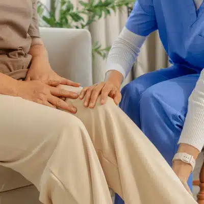 A healthcare provider supports a seated patient’s knee during a knee examination in a clinic setting