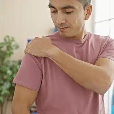 Man touches aching shoulder at home, considering consultation with a shoulder pain specialist for diagnosis