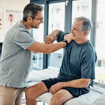 Clinician tests older patient’s shoulder range on table, diagnosing rotator cuff tear dallas symptoms