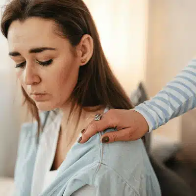 Woman looks down as hand touches shoulder, depicting dallas shoulder fracture discomfort after possible injury