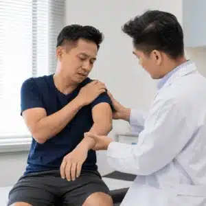 A Dallas shoulder specialist examines a seated patient’s painful shoulder and arm in a bright medical clinic