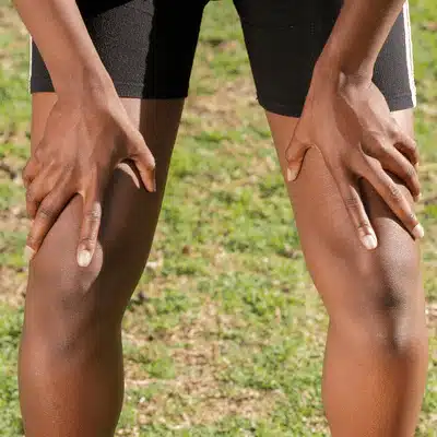 Person holds both knees while standing on grass, considering knee joint pain doctor near me evaluation